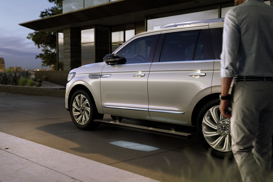 A 2024 Lincoln Navigator SUV with extended running boards is parked in front of a glass house