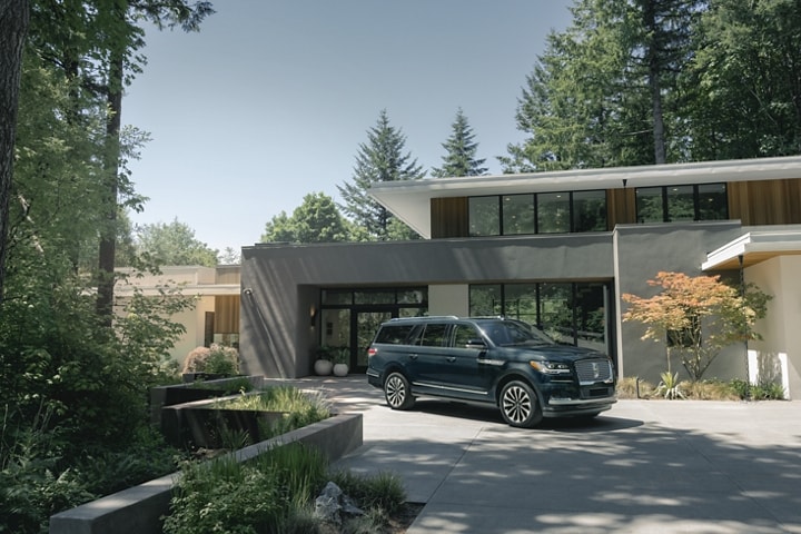 A 2024 Lincoln Navigator SUV is parked in front of a beautiful mid-century modern home on a sunny day