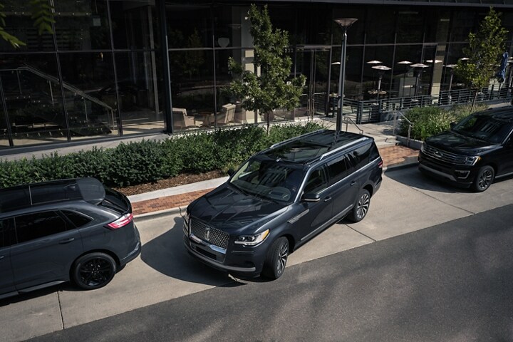 A 2024 Lincoln Navigator SUV is being parked on the side of a downtown street in between two other vehicles