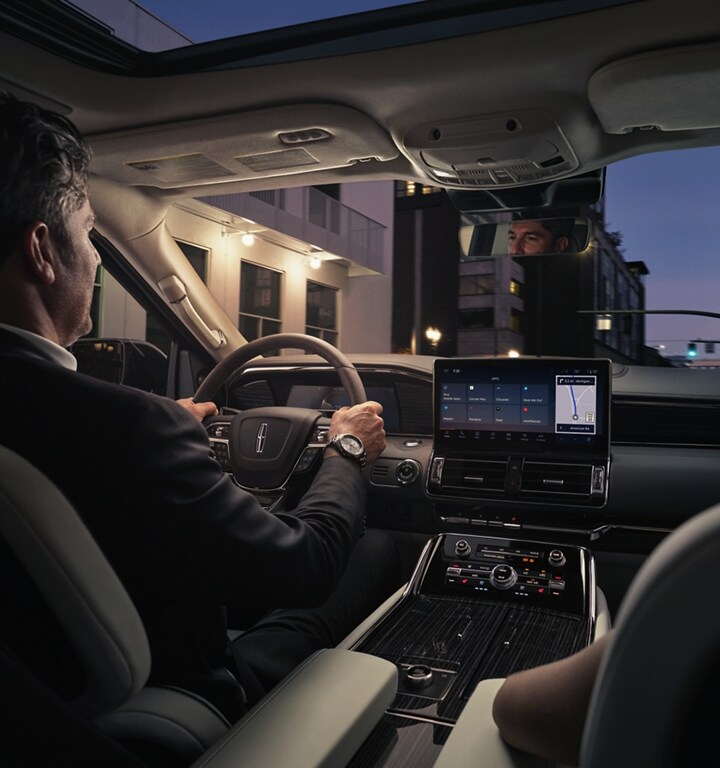 A man and woman are relaxing inside a 2024 Lincoln Navigator SUV as they drive through a downtown street at night