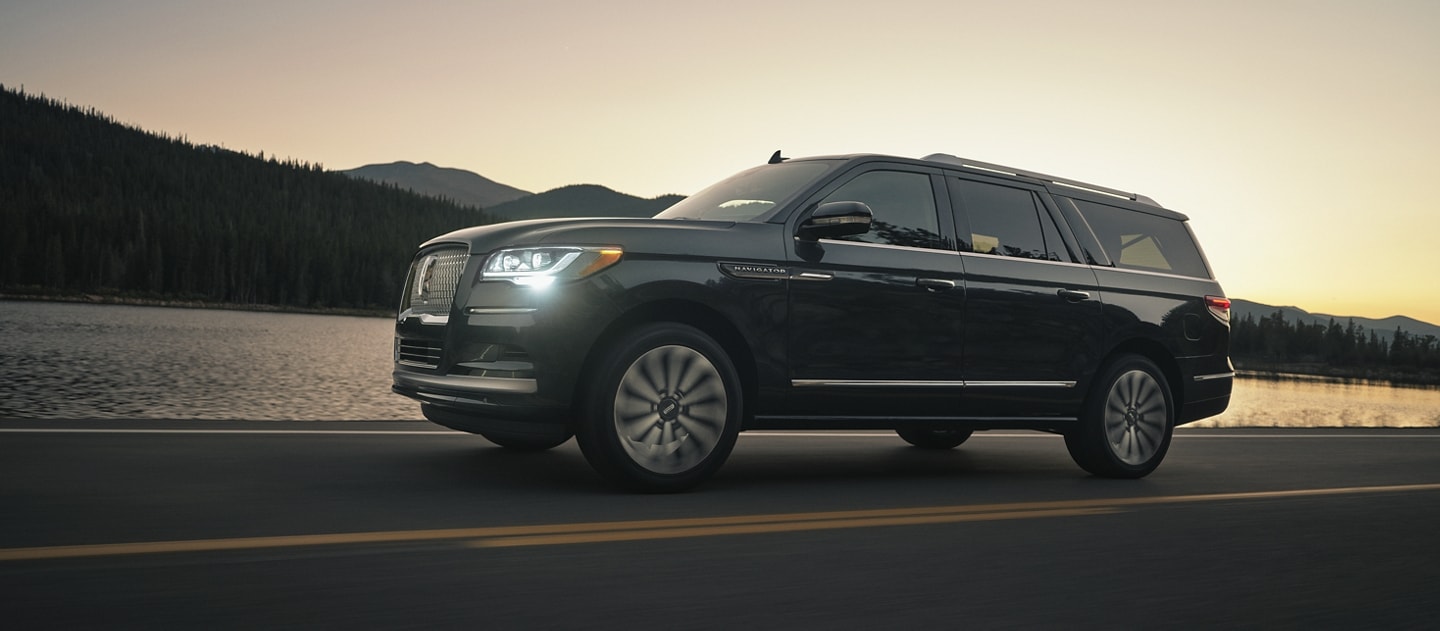 A 2024 Lincoln Navigator SUV is being driven in the mountains at sunset as light bounces off the calm waters