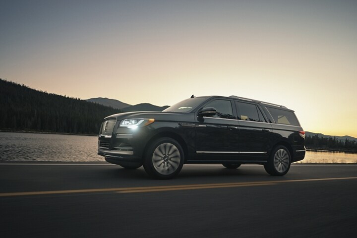 A 2024 Lincoln Navigator SUV is being driven in the mountains at sunset as light bounces off the calm waters