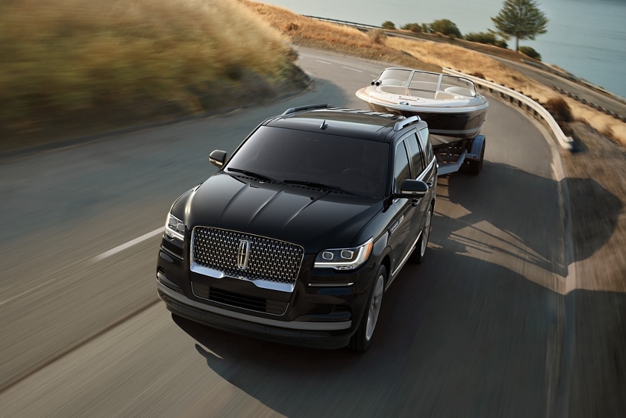 A 2024 Lincoln Navigator® SUV towing a boat is being driven along a curving road