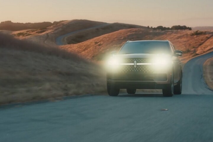 A 2025 Lincoln Navigator® SUV is being driven at dusk with its headlamps illuminated