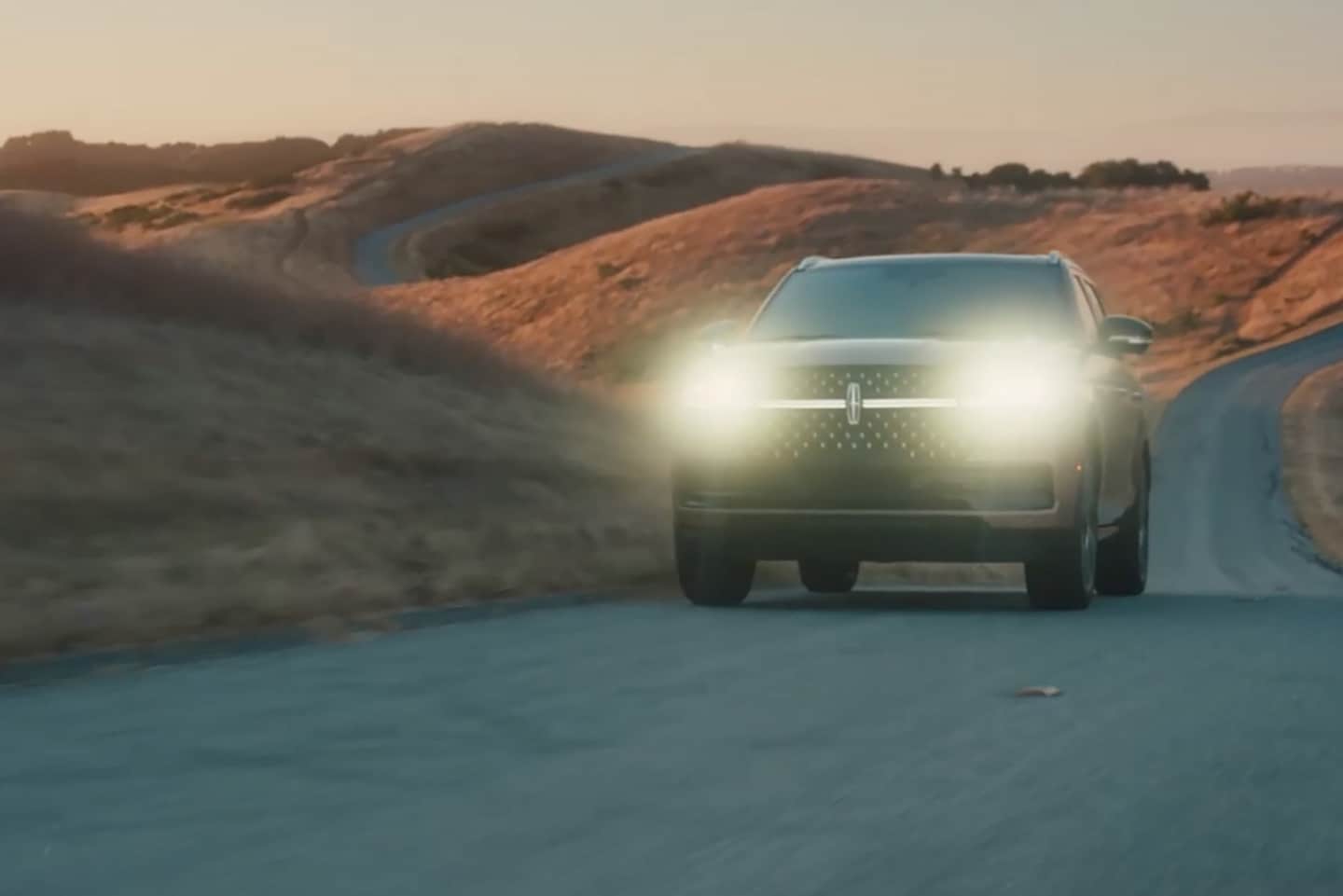 A 2025 Lincoln Navigator is being driven at dusk with its headlamps illuminated